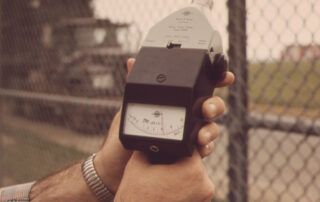 A man's hand holding a noise meter outside the fence of an airport
